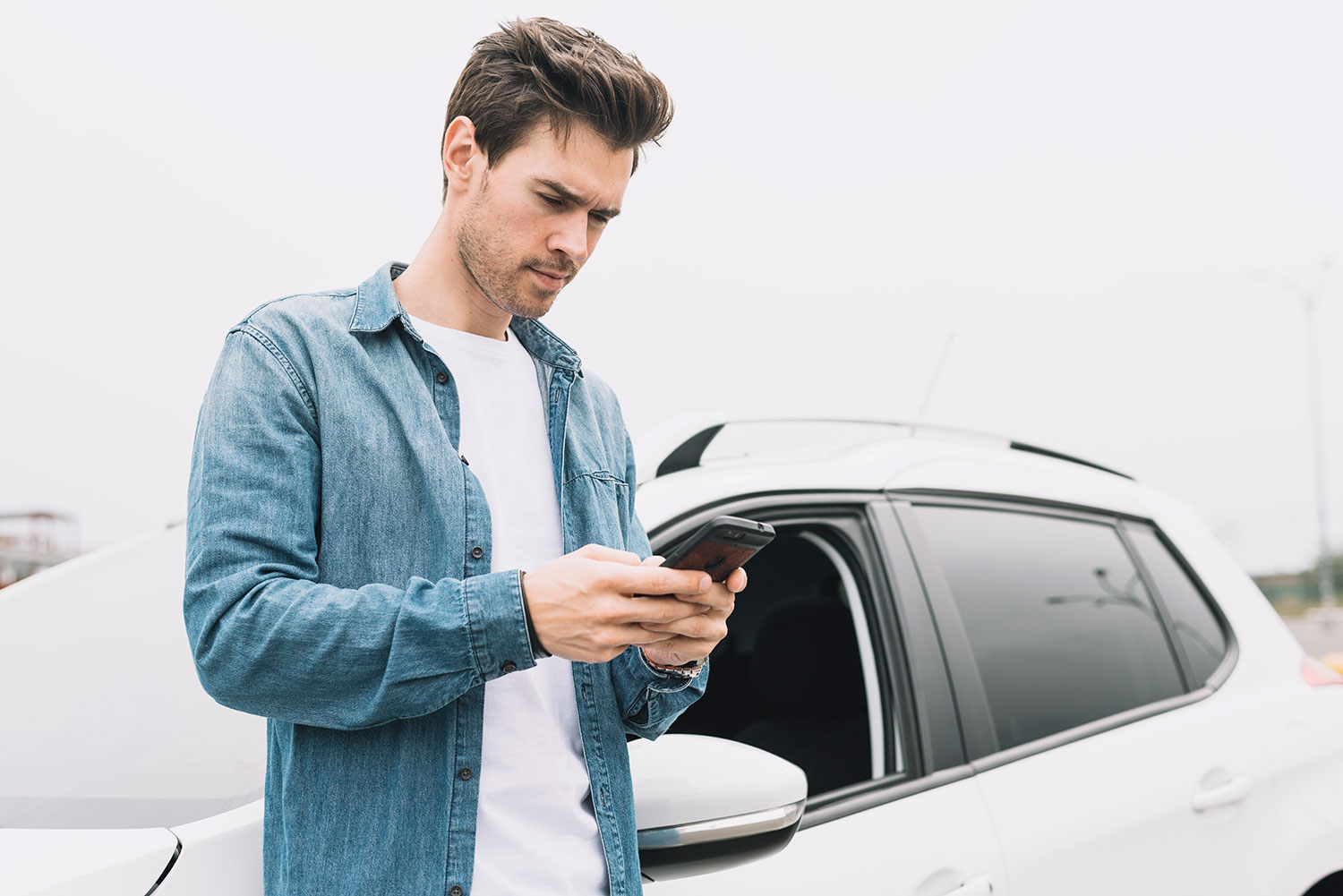 Young man texting message cellphone standing near car window